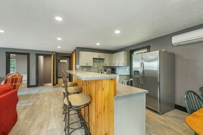 Una cocina moderna con una isla central, taburetes de bar, un refrigerador y un comedor con un sofá rojo y sillas.