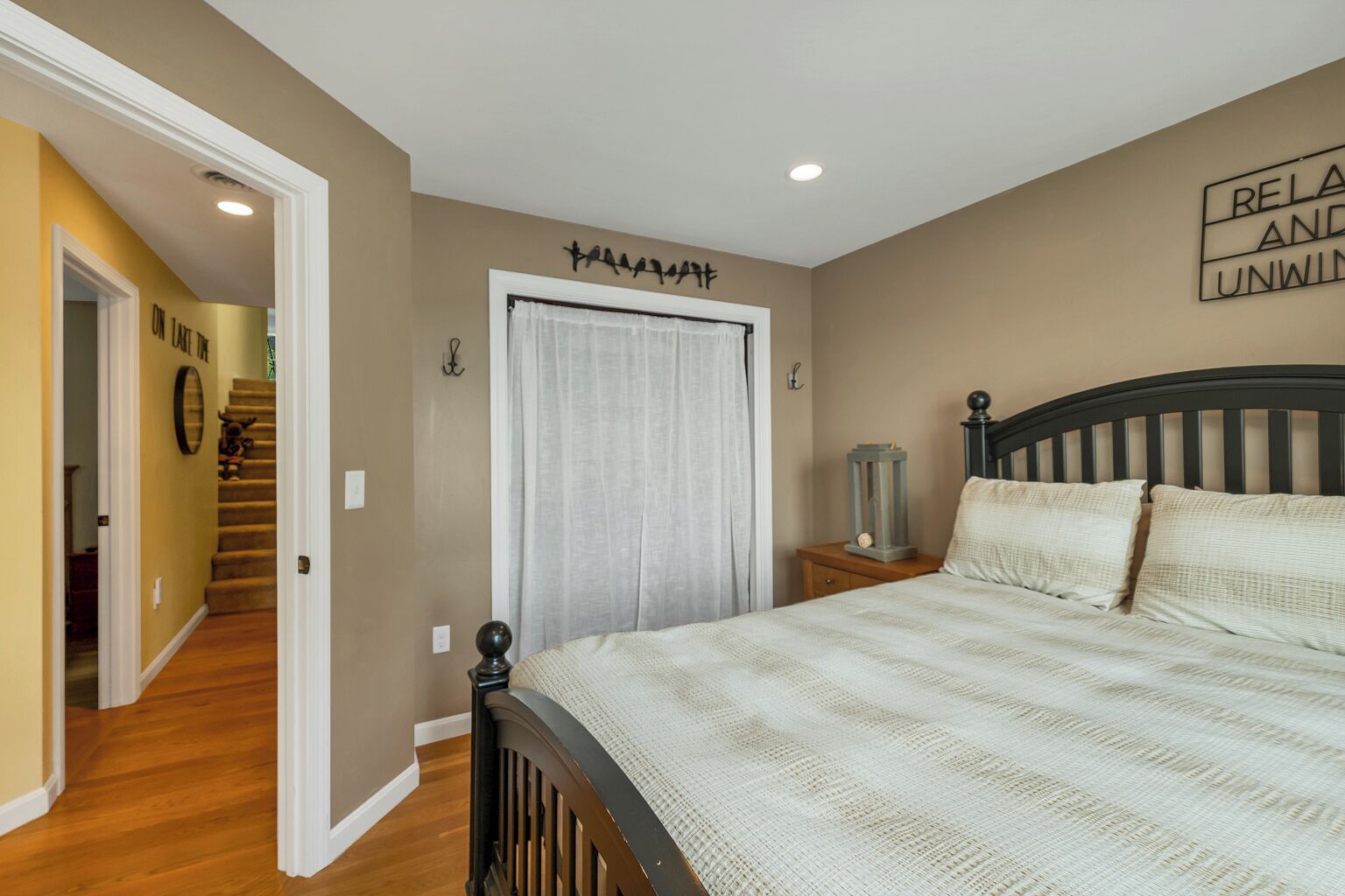 Un dormitorio con cama, mesita de noche, lámpara, puerta y pared con un letrero.