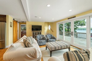 A living room with a sofa, two armchairs, a television, and a view of a lake through large sliding doors. - NEW FOR 2027 Lake Winnipesaukee Waterfront Sleeps 16 (Moultonborough)