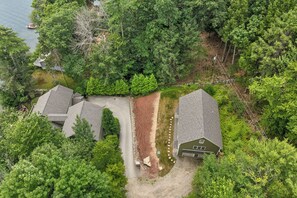 A residential area with two houses, a driveway, and a body of water in the background. - NEW FOR 2027 Lake Winnipesaukee Waterfront Sleeps 16 (Moultonborough)