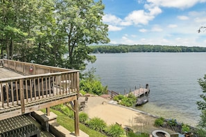 A lakeside property with a wooden deck, outdoor seating, and a dock extending into the water. - NEW FOR 2027 Lake Winnipesaukee Waterfront Sleeps 16 (Moultonborough)