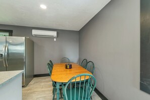 A compact kitchen with a wooden dining table, teal chairs, a stainless steel refrigerator, and a wall-mounted air conditioner. - NEW FOR 2027 Lake Winnipesaukee Waterfront Sleeps 16 (Moultonborough)
