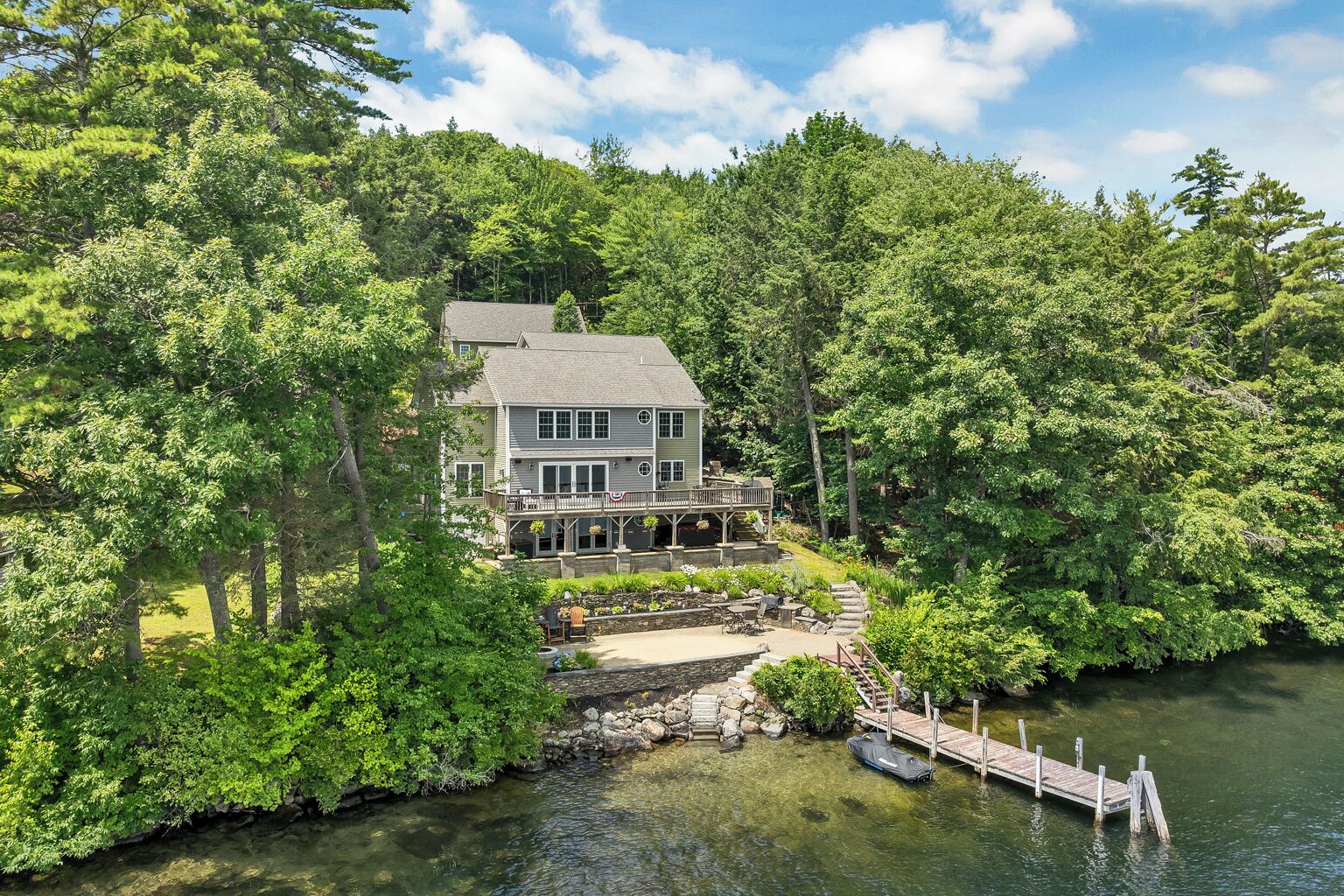 Ein großes Haus mit einer Terrasse und einem Steg, der in einen See führt, umgeben von dichtem Wald.