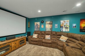 Una sala de cine en casa con una pantalla grande, un sofá de cuero marrón y varios carteles de películas en la pared.