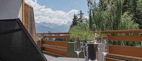 Un balcón con una mesa dispuesta para una comida, con vistas a un paisaje montañoso.