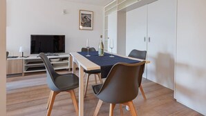 A modern room with a dining table, chairs, a television, and a wardrobe. - Cozy Studio • Swimming Pool • View of the Alps • Crans-Montana (Crans-Montana)