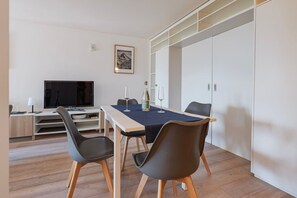 Ein modernes Zimmer mit Esstisch, Stühlen, Fernseher und Kleiderschrank.