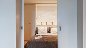 A bedroom with a bed, pillows, a bedside table, and a nightstand. - Cozy Studio • Swimming Pool • View of the Alps • Crans-Montana (Crans-Montana)