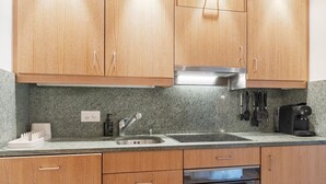 A kitchen with wooden cabinets, a stainless steel sink, a built-in oven, and a coffee maker. - Cozy Studio • Swimming Pool • View of the Alps • Crans-Montana (Crans-Montana)