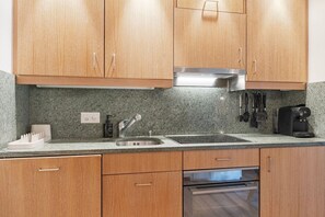 Eine Küche mit Holzausstattung, einer Edelstahl-Spüle, einem Backofen und einer Kaffeemaschine.
