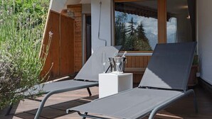 A wooden deck with two lounge chairs and a small table with a glass of water. - Cozy Studio • Swimming Pool • View of the Alps • Crans-Montana (Crans-Montana)