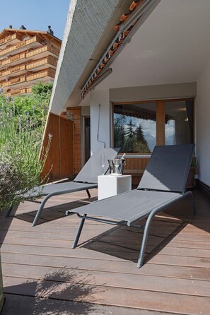 Eine Holzterrasse mit zwei Liegestühlen und einem kleinen Tisch mit einem Glas Wasser.