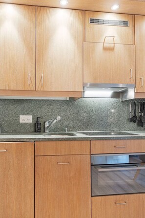 A kitchen with wooden cabinets, a stainless steel range hood, a built-in oven, and a granite countertop. - Cozy Studio • Swimming Pool • View of the Alps • Crans-Montana (Crans-Montana)