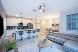 A modern kitchen with a central island, bar stools, a dining area with a sofa, and a ceiling fan. - 4BR w Private Pool Star Wars Room Resort 4993 (Kissimmee)