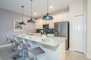 A modern kitchen with a central island, stainless steel appliances, pendant lighting, and a dining area with bar stools. - 4BR w Private Pool Star Wars Room Resort 4993 (Kissimmee)