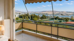 A balcony with a view of a marina, sports fields, and distant mountains. - Floisvos Seaview Escape - Fully Equipped Space (Palaio Faliro)