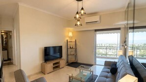 A modern living room with a sofa set, a glass coffee table, a TV, and a view through large windows. - Floisvos Seaview Escape - Fully Equipped Space (Palaio Faliro)