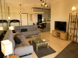 Ein modernes Wohnzimmer mit Sofa, Couchtisch, Fernseher und einer Küche im Hintergrund.
