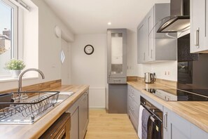 Une cuisine moderne avec un plan de travail en bois, des appareils en acier inoxydable et une horloge bien visible au mur.