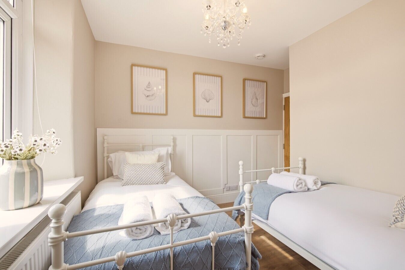 Une chambre d’hôtel avec deux lits, un lustre et des œuvres d’art encadrées accrochées au mur.