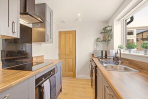 A modern kitchen with wooden countertops, stainless steel appliances, and a window with plants. - Ember Cottage - North East Escapes (Amble)