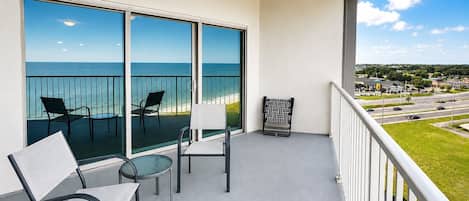 A balcony with a view of the ocean, two chairs, a small table, and a patterned chair.
