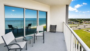 A balcony with a view of the ocean, two chairs, a small table, and a patterned chair. - Sea Breeze 1004 | Overlooks the Beautiful Gulf (Biloxi)