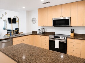A modern kitchen with granite countertops, stainless steel appliances, and wooden cabinets. - Sea Breeze 1004 | Overlooks the Beautiful Gulf (Biloxi)