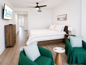A bedroom with a bed, a wooden dresser, a green armchair, a round wooden table, and a ceiling fan. - Sea Breeze 1004 | Overlooks the Beautiful Gulf (Biloxi)