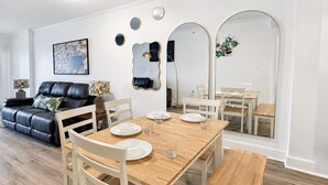Un moderno salón con un sofá de cuero, una mesa de comedor y sillas. Hay espejos decorativos y un cuadro en la pared.