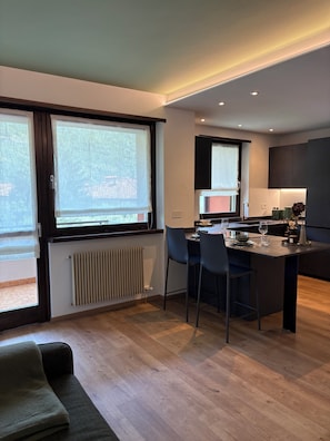 A modern kitchen with a central island, dining chairs, and a view through large windows. - Nido di Rondine Suite Apartments - ALBA (Nago-Torbole)