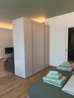 A modern room with a large wardrobe, a flat-screen TV, and neatly folded towels on a table. - Nido di Rondine Suite Apartments - ALBA (Nago-Torbole)