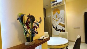 Uma sala de jantar com uma mesa redonda, cadeiras, um vaso com flores e um ar condicionado fixado na parede.