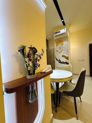 A dining area with a round table, chairs, a vase with flowers, and a wall-mounted air conditioner. - Hamasville Residence (Abuja)