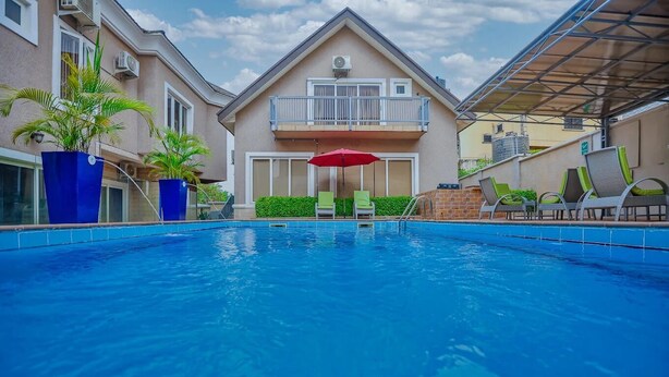 Una piscina con un ombrellone rosso, sedie a sdraio e un edificio con un balcone.
