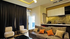 Uma sala de estar moderna com sofá, mesa de centro e área de cozinha ao fundo.