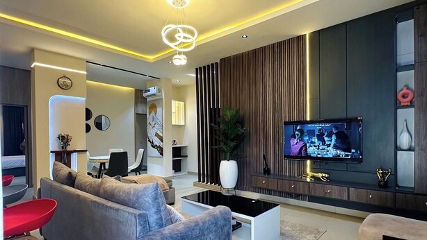Uma sala de estar moderna com um sofá cinzento, uma mesa de centro e uma televisão na parede.
