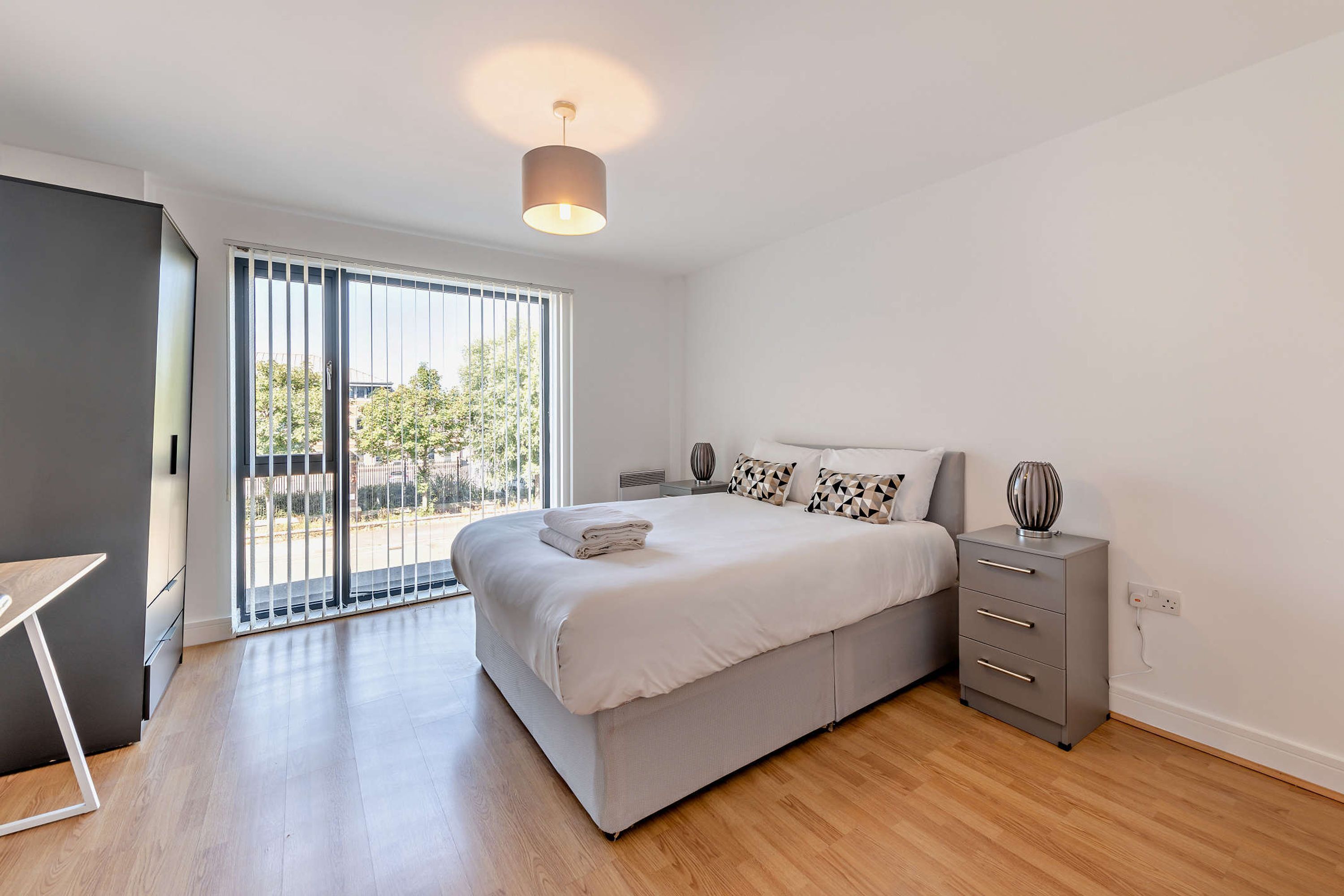 Un dormitorio moderno con una cama grande, una mesita de noche y vistas al exterior a través de una puerta corredera.