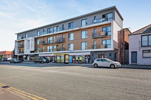 A multi-story building with a ground-level commercial space, multiple balconies, and a parking area.