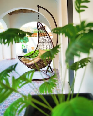 A hanging chair with a woven seat and backrest, suspended from a ceiling by a chain. - Indemela Corfu Lodge  (Karousades)