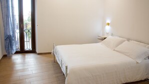Un dormitorio con cama, mesita de noche, lámpara de pared y puerta que da a un balcón.