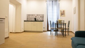 Una cocina compacta con salpicadero de azulejos, un comedor con mesa y sillas, y una pequeña zona de estar con sofá.