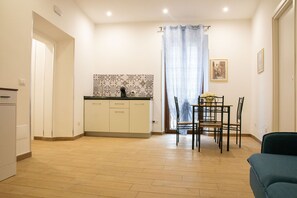A compact kitchen with a tiled backsplash, a dining area with a table and chairs, and a small seating area with a sofa. - Mimì's House: Comfort in the Medieval Village of Nettuno (Nettuno)
