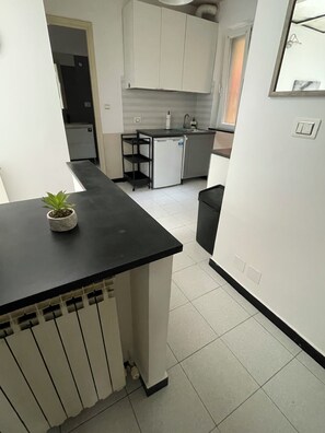 A compact kitchen with a black countertop, white cabinets, and a small island with a plant. - Center in the city of Genoa (Genova)