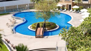 Uma piscina com design circular, rodeada por espreguiçadeiras e guarda-sóis, e uma pequena ponte de acesso à piscina.