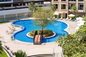 Ein Pool mit kreisförmigem Design, umgeben von Liegestühlen und Sonnenschirmen, mit einer kleinen Brücke, die in den Pool führt.
