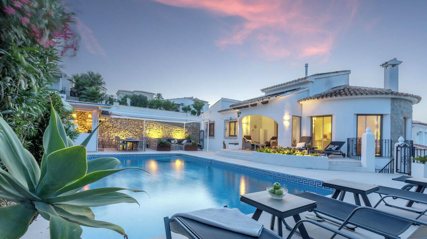 Zona junto a la piscina con sillas de descanso, una mesa y un edificio con fachada de piedra y techo de tejas.