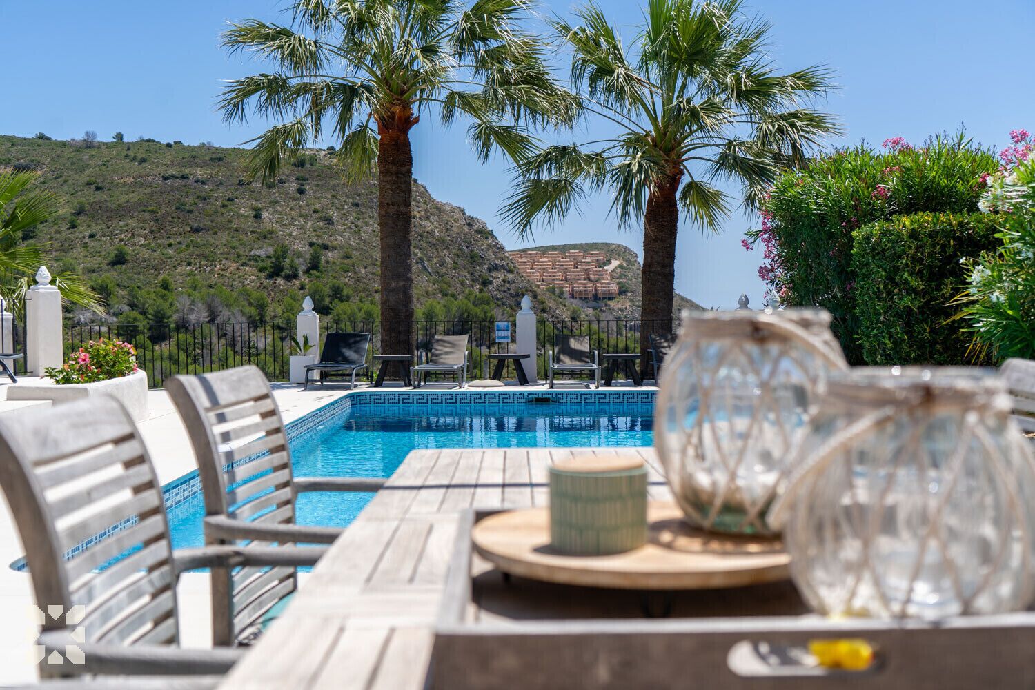 A poolside area with lounge chairs, a table with a vase, and a view of a mountainous landscape.