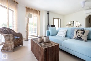A living room with a light blue sofa, a wicker chair, a wooden coffee table, and a lamp. - PALMERAS DEL MAR Villa by Abahana Villas (Teulada)