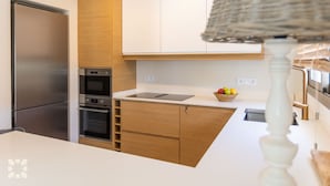 A modern kitchen with a stainless steel refrigerator, built-in oven, and a wooden cabinet structure. - PALMERAS DEL MAR Villa by Abahana Villas (Teulada)